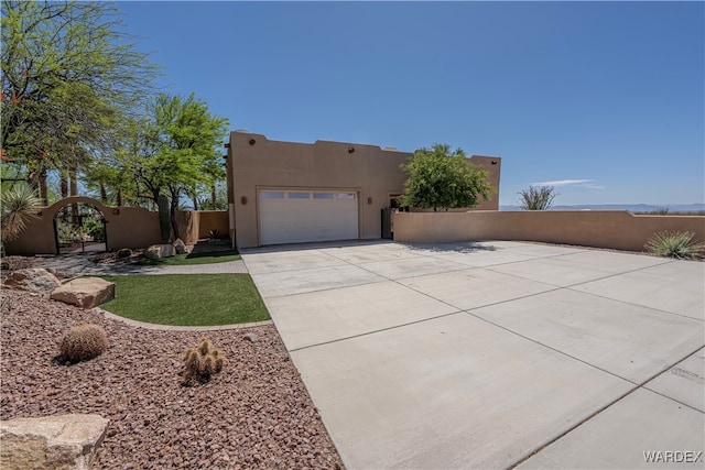 adobe home with a garage, driveway, fence, and stucco siding