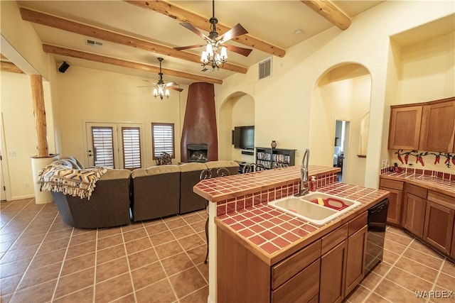 kitchen with tile countertops, visible vents, open floor plan, a sink, and an island with sink