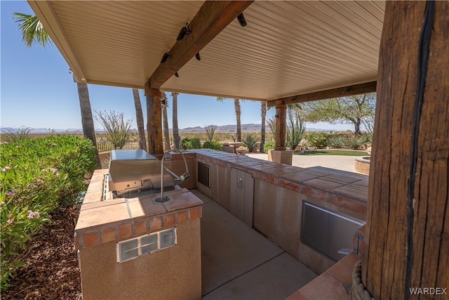 view of patio with exterior kitchen, a grill, and a mountain view