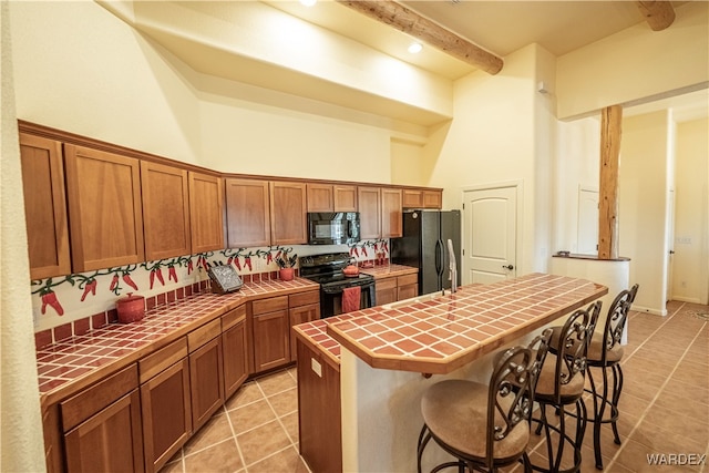 kitchen featuring a center island, brown cabinets, a breakfast bar area, tile counters, and black appliances