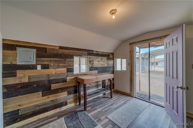 interior space featuring wooden walls, wood finished floors, baseboards, vaulted ceiling, and electric panel