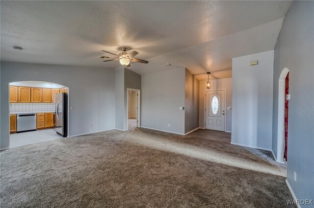 unfurnished living room with ceiling fan, arched walkways, vaulted ceiling, and light colored carpet