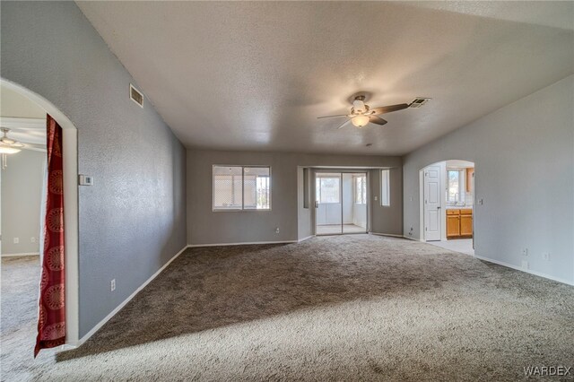 spare room with carpet floors, ceiling fan, visible vents, and arched walkways