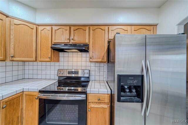 kitchen featuring tile countertops, stainless steel appliances, decorative backsplash, and under cabinet range hood