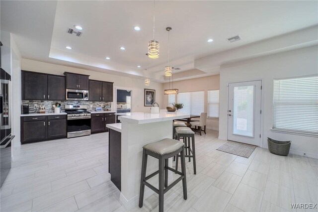 kitchen featuring appliances with stainless steel finishes, a raised ceiling, light countertops, and pendant lighting