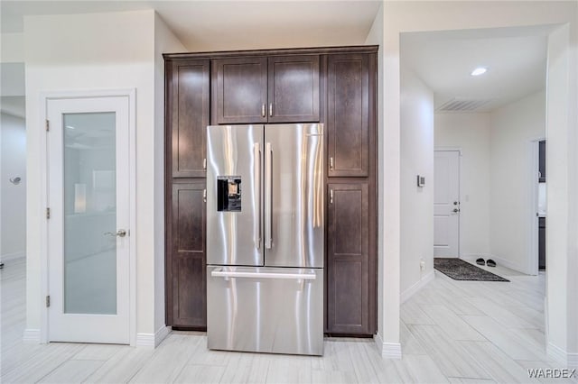 kitchen featuring visible vents, stainless steel fridge, dark brown cabinetry, and baseboards