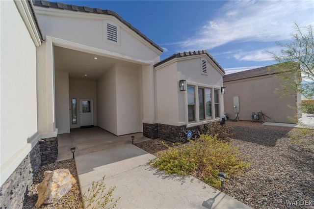 view of exterior entry with stone siding, visible vents, and stucco siding