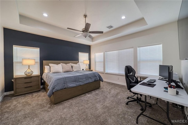 carpeted bedroom with visible vents, multiple windows, a tray ceiling, and baseboards