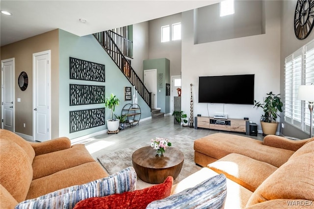 living room featuring baseboards, a healthy amount of sunlight, stairway, and a towering ceiling
