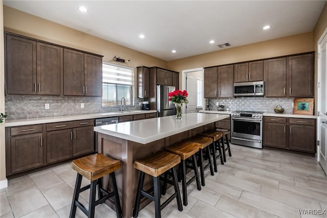 kitchen featuring a kitchen island, dark brown cabinets, a sink, a breakfast bar, and stainless steel appliances
