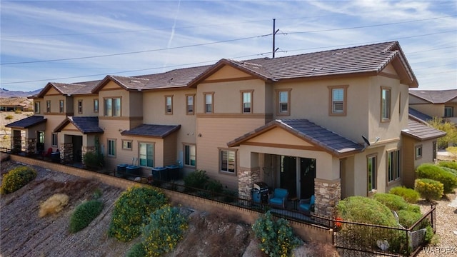 rear view of property featuring a tile roof, stone siding, and stucco siding