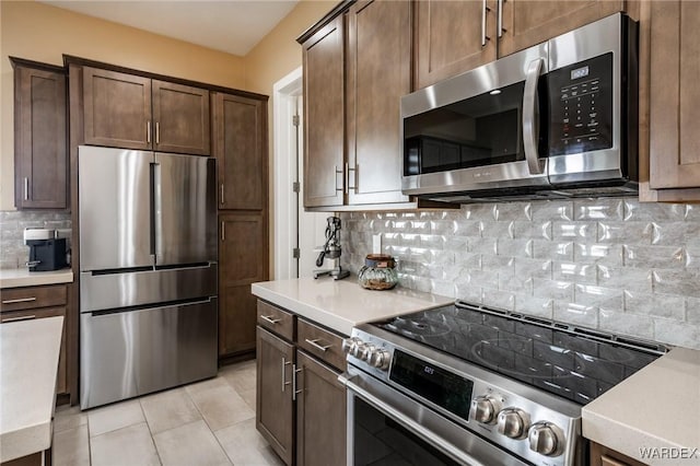 kitchen featuring dark brown cabinetry, light countertops, tasteful backsplash, light tile patterned floors, and stainless steel appliances