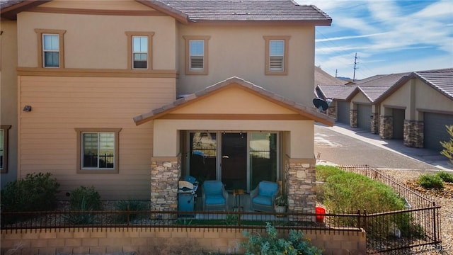 rear view of property featuring a tiled roof, fence, stone siding, and stucco siding