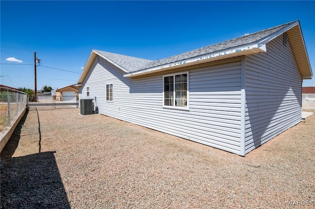 view of property exterior with a shingled roof, fence, and central air condition unit