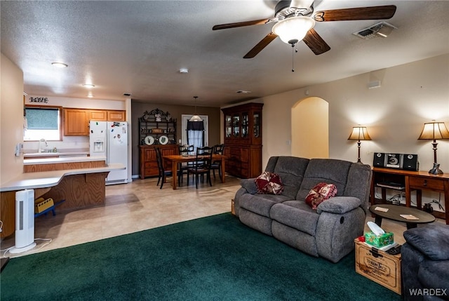 living area with visible vents, arched walkways, ceiling fan, and light colored carpet