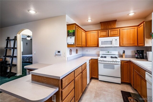 kitchen featuring arched walkways, a peninsula, white appliances, light countertops, and brown cabinets