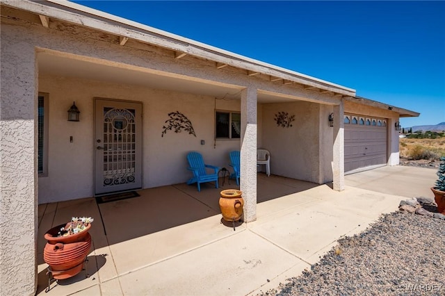 doorway to property with concrete driveway, an attached garage, and stucco siding