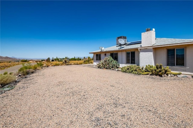 exterior space featuring roof mounted solar panels, a chimney, and stucco siding