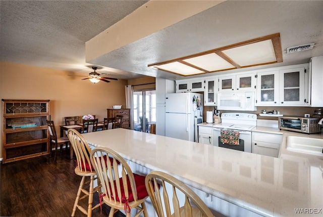 kitchen with white appliances, visible vents, white cabinets, glass insert cabinets, and light countertops