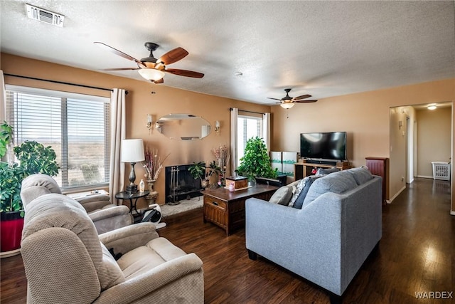 living area featuring dark wood-style floors, a fireplace with raised hearth, a textured ceiling, and visible vents