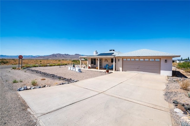 view of front of house featuring a mountain view, covered porch, a garage, driveway, and roof mounted solar panels