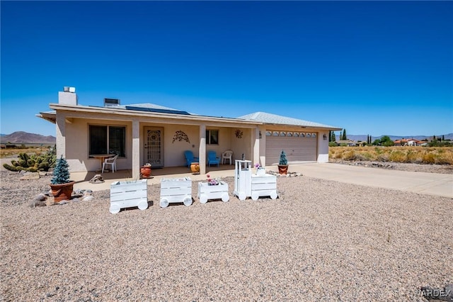 ranch-style home featuring a garage, driveway, a chimney, a mountain view, and stucco siding