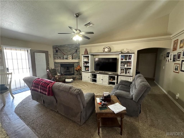living room with visible vents, arched walkways, a stone fireplace, ceiling fan, and vaulted ceiling