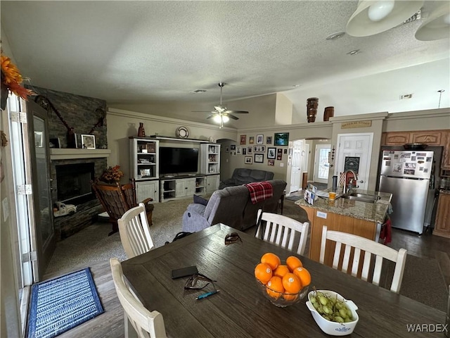dining room featuring a fireplace, dark wood finished floors, a textured ceiling, a ceiling fan, and vaulted ceiling