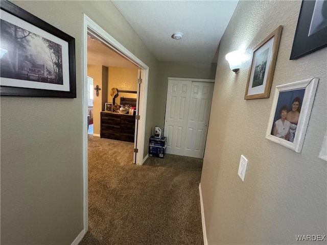hall featuring a textured wall, carpet flooring, and baseboards
