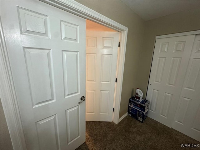 corridor featuring dark carpet and baseboards