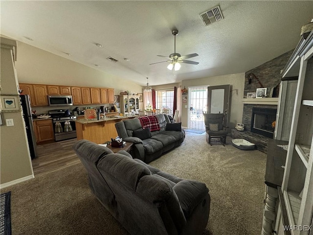 living area with a stone fireplace, a ceiling fan, visible vents, and lofted ceiling