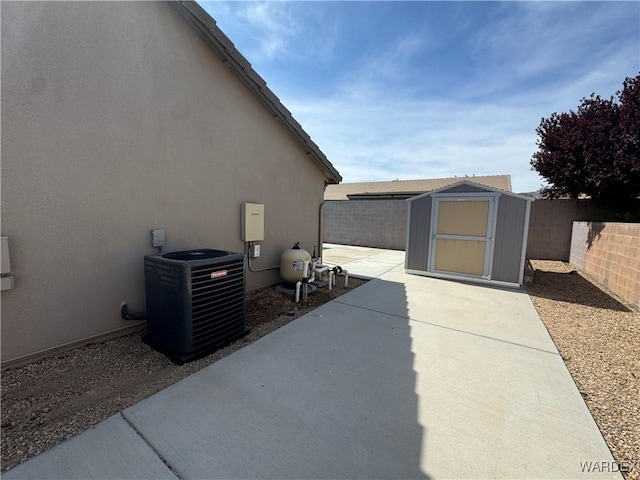 view of patio / terrace with central air condition unit, an outbuilding, a storage unit, and a fenced backyard