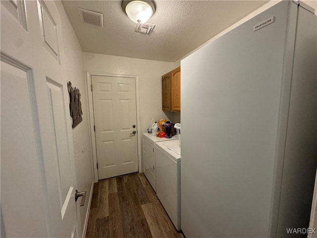 clothes washing area featuring washer and dryer, visible vents, cabinet space, and dark wood-style flooring
