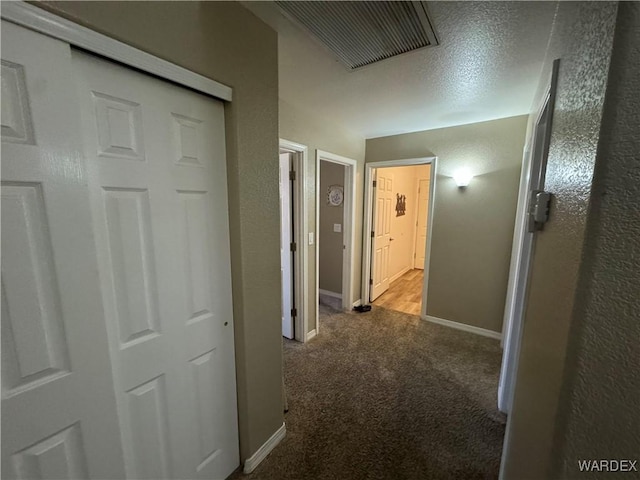 corridor featuring a textured wall, visible vents, baseboards, and carpet floors