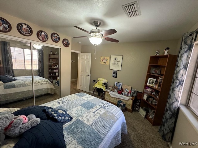 bedroom featuring a closet, a textured ceiling, carpet floors, visible vents, and ceiling fan