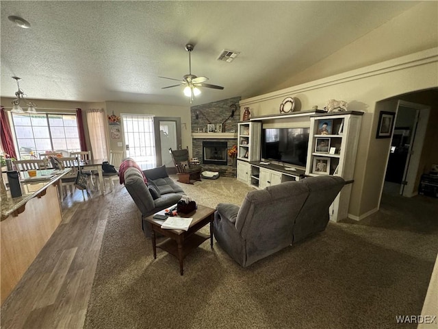 living area featuring lofted ceiling, a fireplace, a textured ceiling, visible vents, and ceiling fan