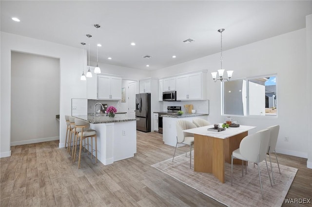 kitchen with a kitchen breakfast bar, a center island, decorative light fixtures, stainless steel appliances, and white cabinetry