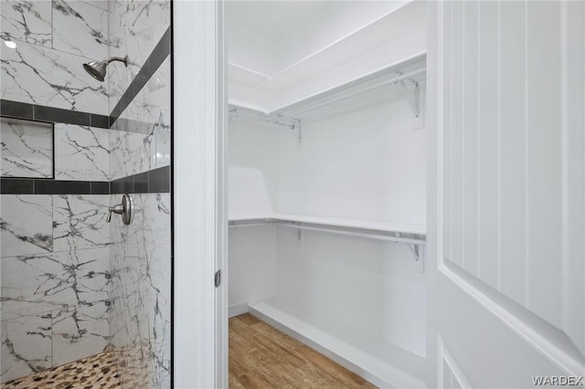 bathroom featuring a spacious closet, wood finished floors, and a marble finish shower