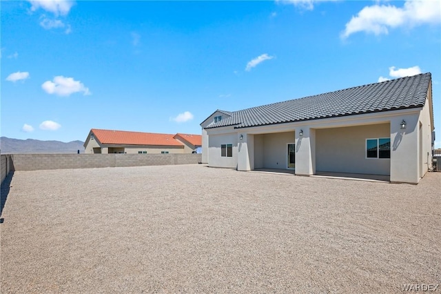 back of property with a patio, a mountain view, fence, a tile roof, and stucco siding