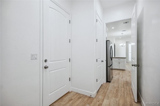 hall featuring light wood finished floors, visible vents, baseboards, and a chandelier