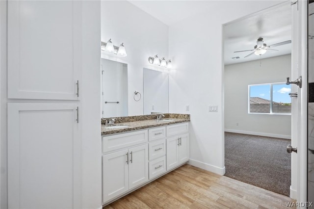 full bathroom featuring ceiling fan, wood finished floors, a sink, baseboards, and double vanity