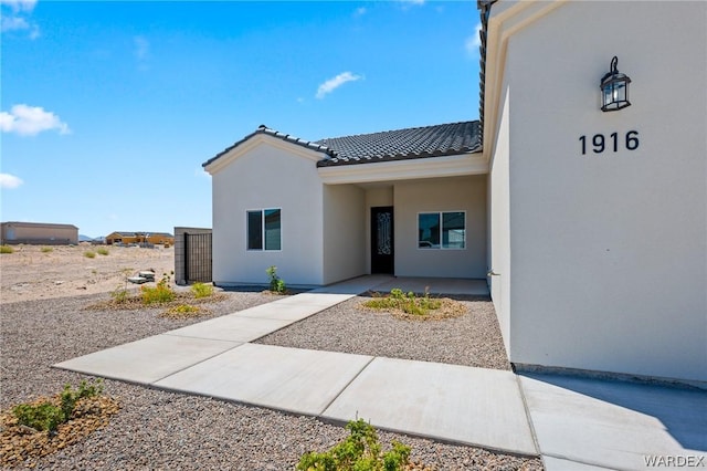 view of exterior entry with a tiled roof and stucco siding