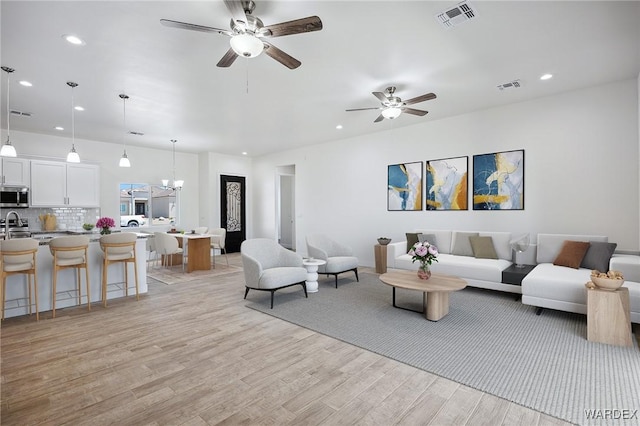 living room featuring recessed lighting, visible vents, light wood finished floors, and ceiling fan with notable chandelier