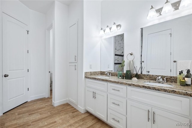 bathroom with double vanity, a sink, toilet, and wood finished floors