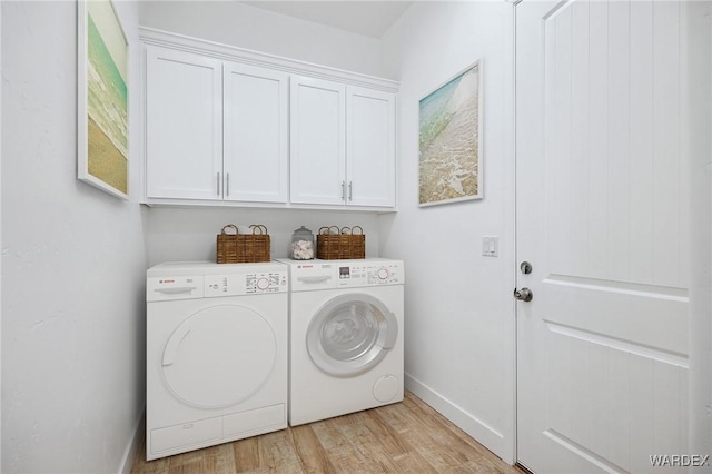 laundry area with baseboards, light wood finished floors, cabinet space, and washer and dryer