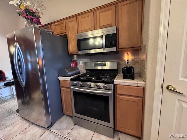 1481 E Topaz Cir Unit 2, Fort Mohave, AZ 86426 - kitchen featuring light tile patterned floors, brown cabinetry, decorative backsplash, tile counters, and stainless steel appliances