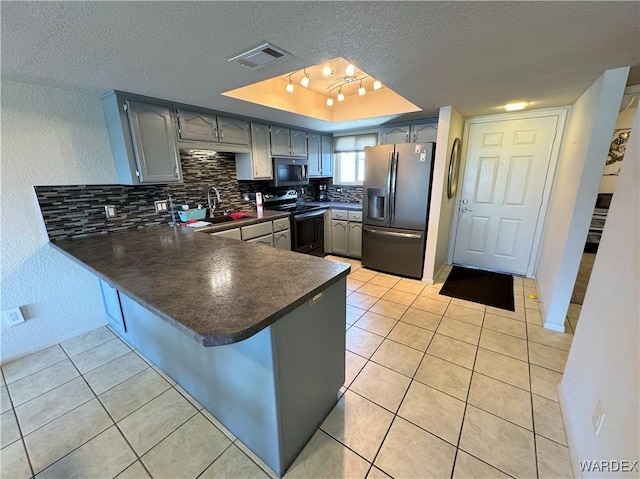 kitchen with a textured ceiling, stainless steel appliances, a peninsula, visible vents, and a raised ceiling