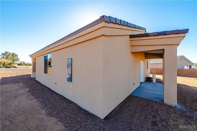 view of side of property featuring a patio area, fence, and stucco siding