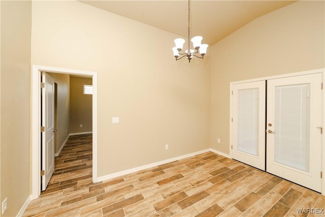 spare room with a chandelier, high vaulted ceiling, wood finish floors, and baseboards