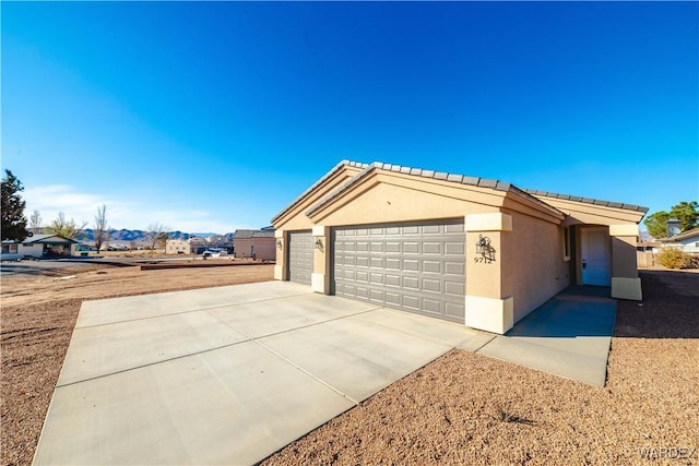 view of side of home featuring driveway, an attached garage, a tiled roof, and stucco siding